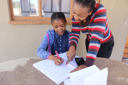 A student receiving a ConnectEd tutorial from her home in Gaborone, Botswana. Her mother supports her lesson while listening to guidance from the facilitator on the phone.  Credit: Chisala Mipata, Youth Impact